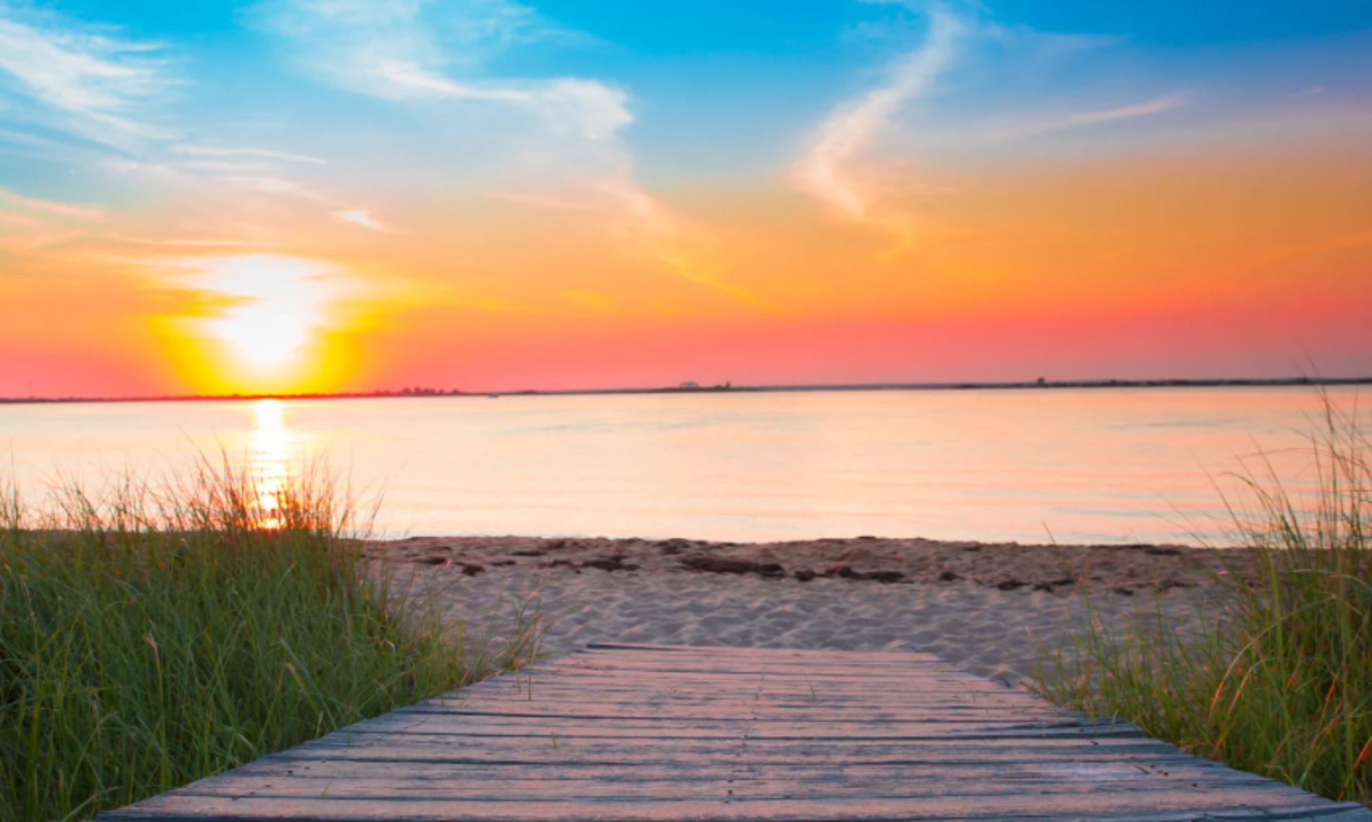 a picture of a pathway leading to the beach under a stunning orange and pink sunset